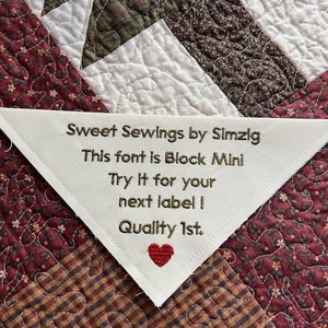 May include: A white triangular fabric label with gold embroidery that reads "Sweet Sewings by Simzig", "This font is Block Mini", "Try It for your next label I", and "Quality 1st." A red heart is embroidered below the text.