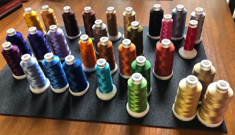 May include: A collection of spools of embroidery thread in various colours, including gold, blue, green, red, and purple. The spools are arranged on a black surface.