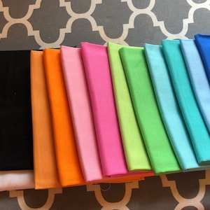May include: A collection of 12 fabric swatches in various colours, including white, black, orange, pink, hot pink, lime green, light blue, sky blue, royal blue, lavender, and purple.