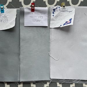 May include: Four fabric swatches in different shades of grey. The swatches are labelled with the fabric name, colour, and number. The swatches are arranged from lightest to darkest.
