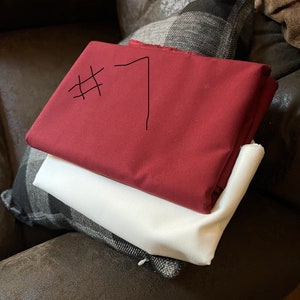 May include: Two pieces of fabric, one red and one white, are stacked on top of each other. The red fabric has the number "#7" written on it in black marker.