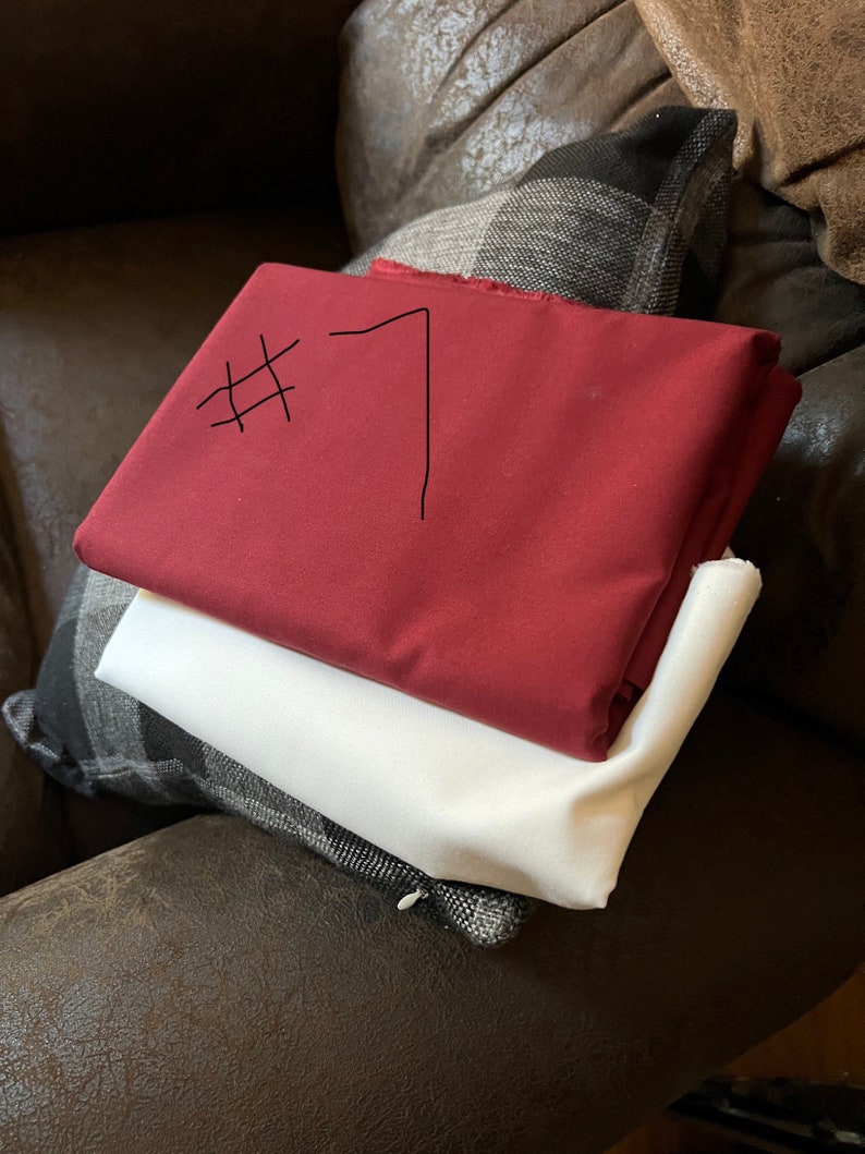 May include: Two pieces of fabric, one red and one white, are stacked on top of each other. The red fabric has the number "#7" written on it in black marker.