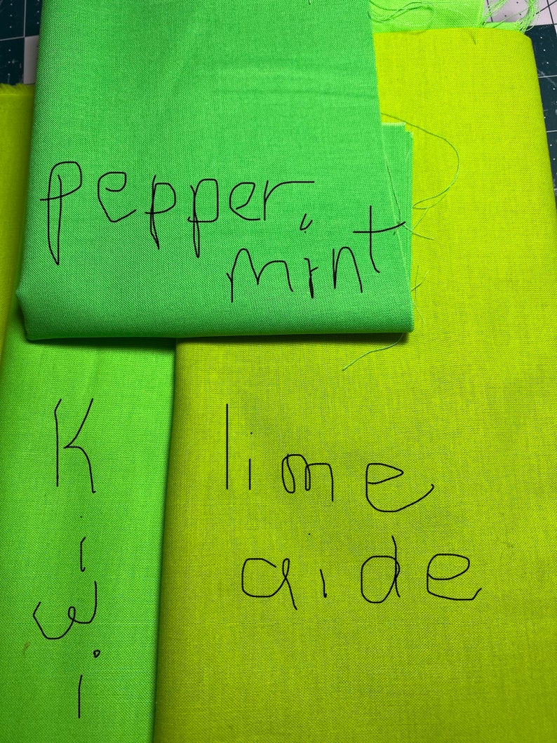 May include: Two pieces of fabric, one green and one yellow-green. The green fabric has the text "pepper mint" written on it. The yellow-green fabric has the text "lime aide" written on it.