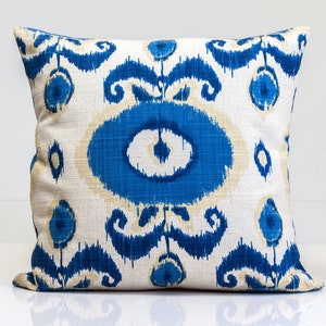 May include: A white throw pillow with a blue and white ikat pattern. The pillow has a square shape and is made of a soft, textured fabric.