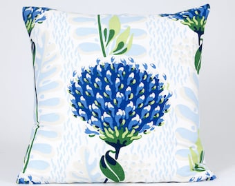 Puede incluir: Una almohada blanca con un patrón floral azul y verde. La almohada presenta una gran flor azul con hojas y tallos verdes.