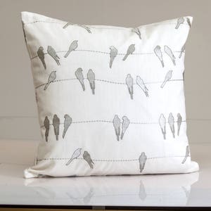 May include: White throw pillow with a gray embroidered design of birds on a wire.