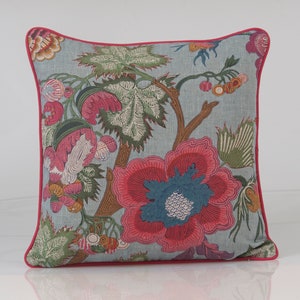 Pode incluir: Uma almofada de lançamento azul e rosa com padrão floral e uma borda rosa. A almofada apresenta uma grande flor rosa com um centro azul e folhas verdes.