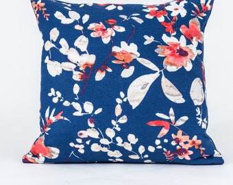 Puede incluir: Una almohada azul con un patrón floral blanco y rojo. La almohada está hecha de una tela suave y texturizada.