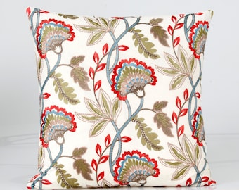 Op de afbeelding: Een wit kussen met een geborduurd bloemenpatroon in rood, blauw en groen. Het kussen heeft een herhalend ontwerp van gestileerde bloemen en bladeren.