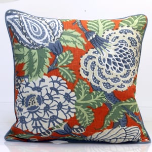 May include: Square decorative pillow with a vibrant floral pattern. The pillow features large white and blue flowers, green leaves, and a blue border against a red-orange background. The design is reminiscent of a botanical print.