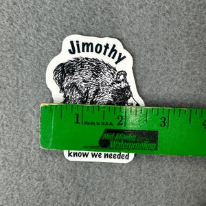 May include: A white die-cut sticker featuring a black and white illustration of a raccoon with the text Jimothy above and know we needed below. A green ruler is placed across the sticker, showing a width of approximately 3.25 inches.