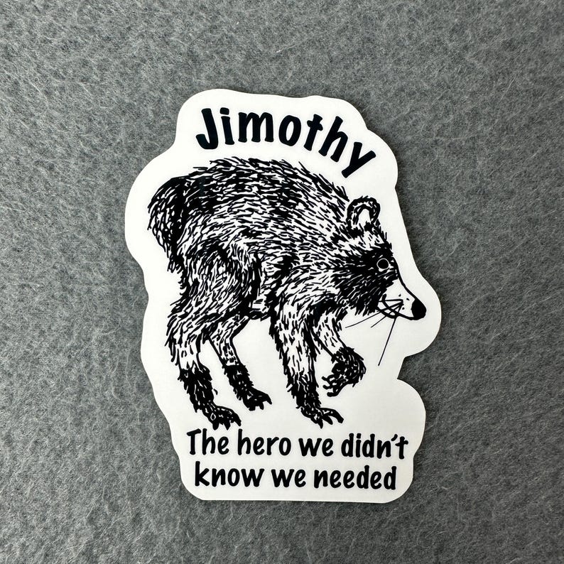 May include: A white die-cut sticker featuring a black and white ink-style illustration of a raccoon. The text "Jimothy" is printed above the animal, and the phrase "The hero we didn't know we needed" is printed below in a black sans-serif font.