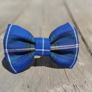 Peut inclure: Un nœud papillon bleu à carreaux avec des accents blancs, verts et rouges. Le nœud papillon est en tissu et est présenté sur une surface en bois. Accessoire pour événements formels.