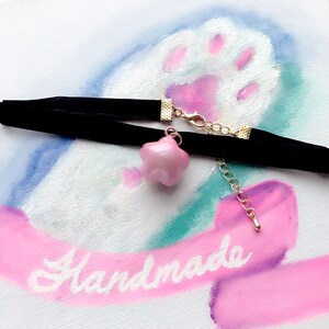Peut inclure: Un collier ras du cou en velours noir avec un pendentif en forme d'&eacute;toile rose. Le collier est dot&eacute; de fermoirs en m&eacute;tal dor&eacute; et d'une cha&icirc;ne d'extension. Le mot "Handmade" est visible en arri&egrave;re-plan.