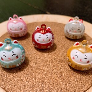 Peut inclure: Cinq figurines rondes de chat color&eacute;es avec un visage souriant et une boucle pour suspendre. Les figurines sont dans des tons de rose, rouge, vert, or et gris. Les figurines de chat sont sur une surface en bois.