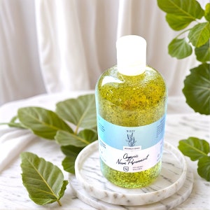 May include: A clear glass bottle of organic neem peppermint bodywash with a white cap. The bottle is sitting on a white marble coaster. The bottle has a green label with the text "Nizzy Bodywash Series Organic Neem Peppermint 100% Organic 250 ml"