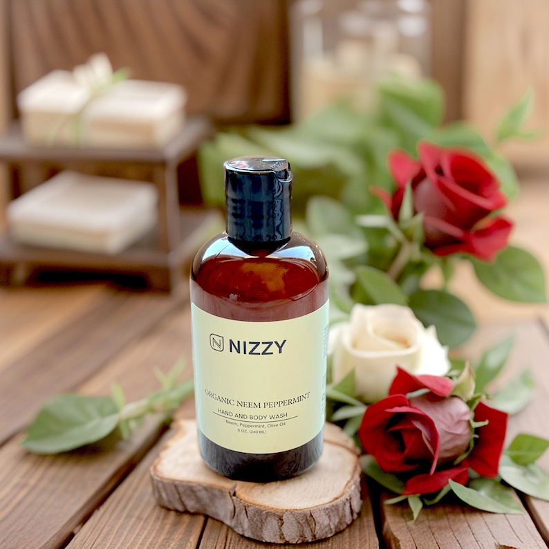 May include: A brown bottle of "Nizzy" Organic Neem Peppermint Hand and Body Wash. The bottle is sitting on a wooden surface with red and white roses.