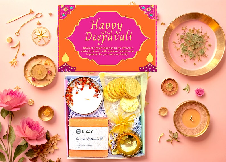 May include: A gift box with a pink and orange lid that says 'Happy Deepavali' with a message about decorating the sunrise with wishes of success and happiness. The box contains a white candle with dried flowers, a small bag of gold coins, a bar of orange oatmeal soap, and a small gold diya.