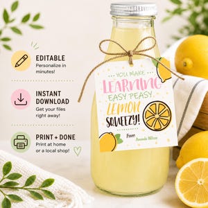 Może przedstawiać: Przezroczysta szklana butelka wypełniona żółtym płynem, ozdobiona etykietą z napisem "You Make Learning Easy Peasy Lemon Squeezy!" z grafiką cytryny. Etykieta jest zawiązana sznurkiem. Świeże cytryny w tle.