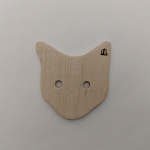 Puede incluir: Un bol de lana de madera con forma de gato con dos agujeros para la lana y un pequeño logotipo de bicicleta en la parte superior.