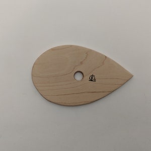 May include: A light wood sculpting tool shaped like a teardrop with a hole in the center. The tool has a small logo of a bicycle on the side.