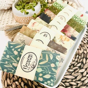 May include: A collection of colorful beeswax food wraps with floral and geometric patterns. The wraps are packaged with a label that reads "Beeswax Wrap".