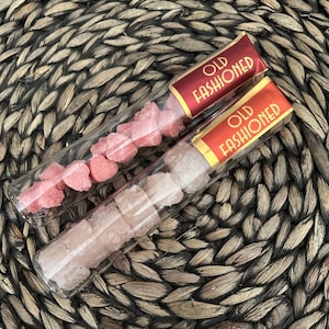 May include: Two glass tubes filled with pink and white sugar cubes. The tubes have labels that say "Old Fashioned".