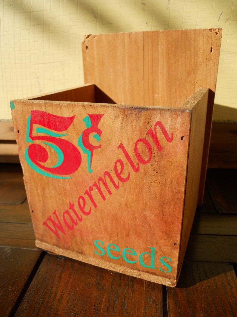 May include: A wooden box with the words "5&cent; Watermelon Seeds" painted on it in red and green.