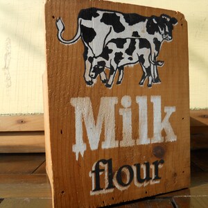 May include: A wooden box with a black and white illustration of two cows and the text "Milk flour" painted on the front.