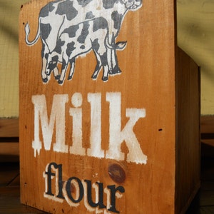 May include: A wooden box with a black and white illustration of two cows. The box is labeled "Milk flour".