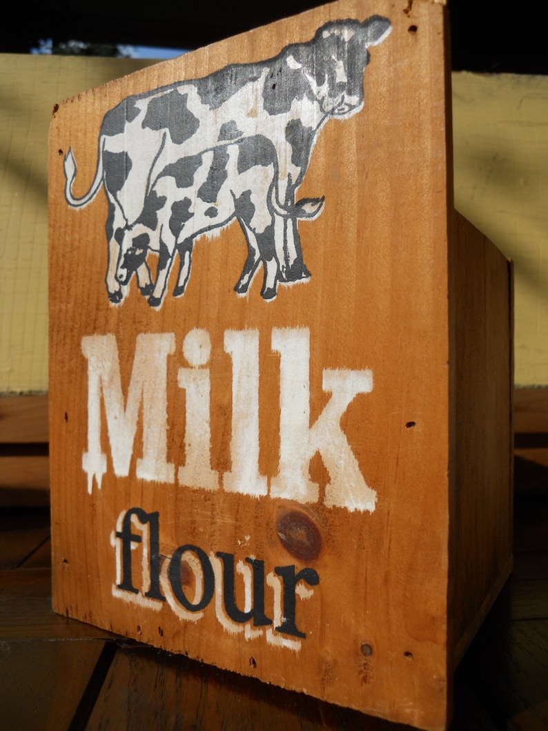 May include: A wooden box with a black and white illustration of two cows. The box is labeled "Milk flour".