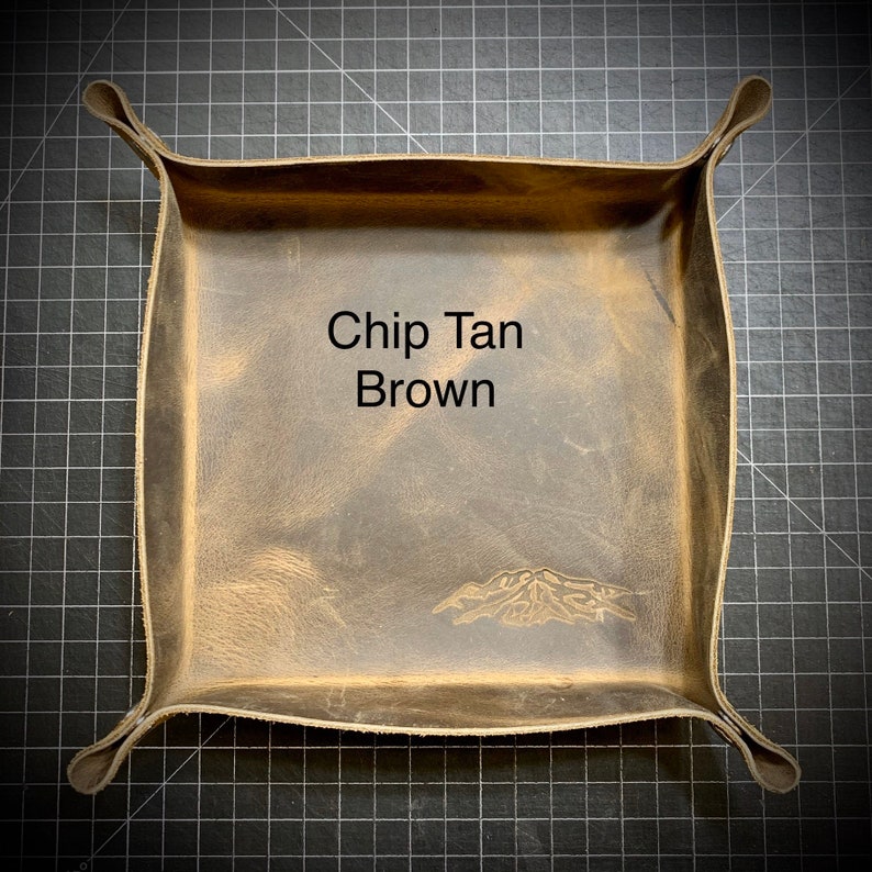 Puede incluir: Una bandeja de cuero marr&oacute;n con un dise&ntilde;o de monta&ntilde;a y el texto "Chip Tan Brown" en el centro.