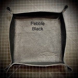 Puede incluir: Una bandeja de cuero negro con textura de guijarro. La bandeja tiene forma cuadrada con esquinas redondeadas y un borde elevado. El texto "Pebble Black" est&aacute; impreso en la bandeja.