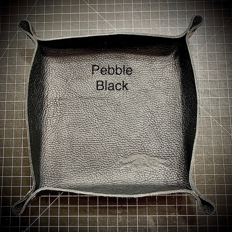 Puede incluir: Una bandeja de cuero negro con textura de guijarro. La bandeja tiene forma cuadrada con esquinas redondeadas y un borde elevado. El texto "Pebble Black" est&aacute; impreso en la bandeja.