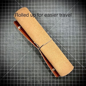Puede incluir: Una estera de cuero marr&oacute;n enrollada con una superficie de gamuza beige. La estera est&aacute; atada con una cuerda y tiene remaches met&aacute;licos en los bordes. "Enrollado para un viaje m&aacute;s f&aacute;cil" est&aacute; escrito en blanco en la estera.