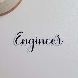 May include: A white background with a small potted cactus in the top left corner. The word "Engineer" is written in black cursive on a white sticker in the center of the image.