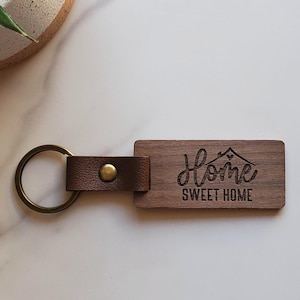 May include: A wooden keychain with a brown leather strap. The keychain has the words "Home Sweet Home" engraved on it.