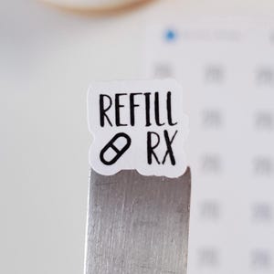 May include: White sticker with black text that says "REFILL RX" with a small pill icon. The sticker is attached to a silver metal bar.
