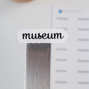 May include: A white sticker with the word "museum" written in black cursive script.