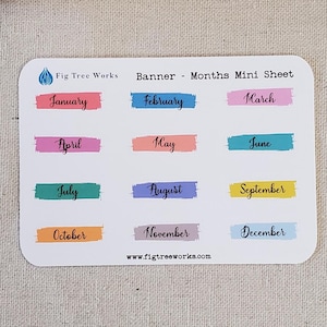 May include: A sheet of colorful mini banners with the months of the year printed on them. The banners are in different colors, including pink, blue, green, orange, and purple. The text "Fig Tree Works Banner - Months Mini Sheet" is printed at the top of the sheet. The website address "www.figtreeworks.com" is printed at the bottom of the sheet.