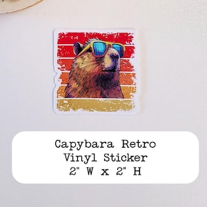 May include: A retro-style vinyl sticker featuring a capybara wearing sunglasses against a sunset background. The sticker is 2 inches wide by 2 inches high. "Capybara Retro Vinyl Sticker 2" W x 2" H" is printed below the image.