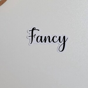 May include: A white sticker with the word "fancy" written in black cursive script.