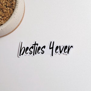May include: A white sticker with the text "besties 4ever" written in black cursive font. A small potted cactus plant is in the upper left corner of the image.
