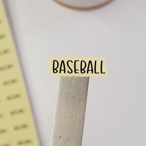 May include: A yellow sticker with the word "BASEBALL" written in black.