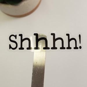 May include: A clear sticker with the text "shhhh!" printed in black.