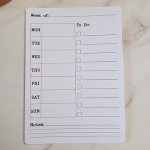 May include: A white weekly planner with the text "Week of:" and "To Do:" printed at the top. The days of the week are listed down the left side, with checkboxes for each day. There is a space for notes at the bottom.