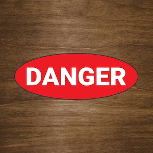May include: A red oval sign with the word "DANGER" in white letters on a brown wooden background.