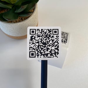 May include: A white square sticker with a black QR code on it. The sticker is attached to a blue pen.