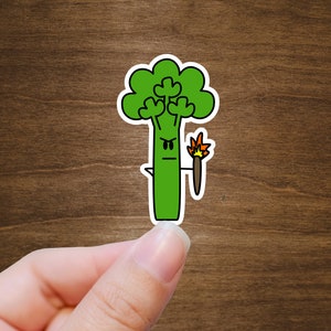 May include: A green cartoon broccoli with an angry face holding a burning stick. The broccoli is on a brown wooden background.