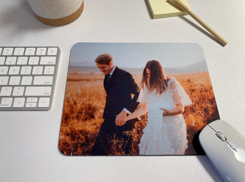 May include: A couple in wedding attire walks through a field of tall grass. The groom is wearing a dark suit and the bride is wearing a white dress. The background is a hazy sunset.